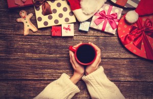 Female holding cup of coffee on wooden table near christmas gift